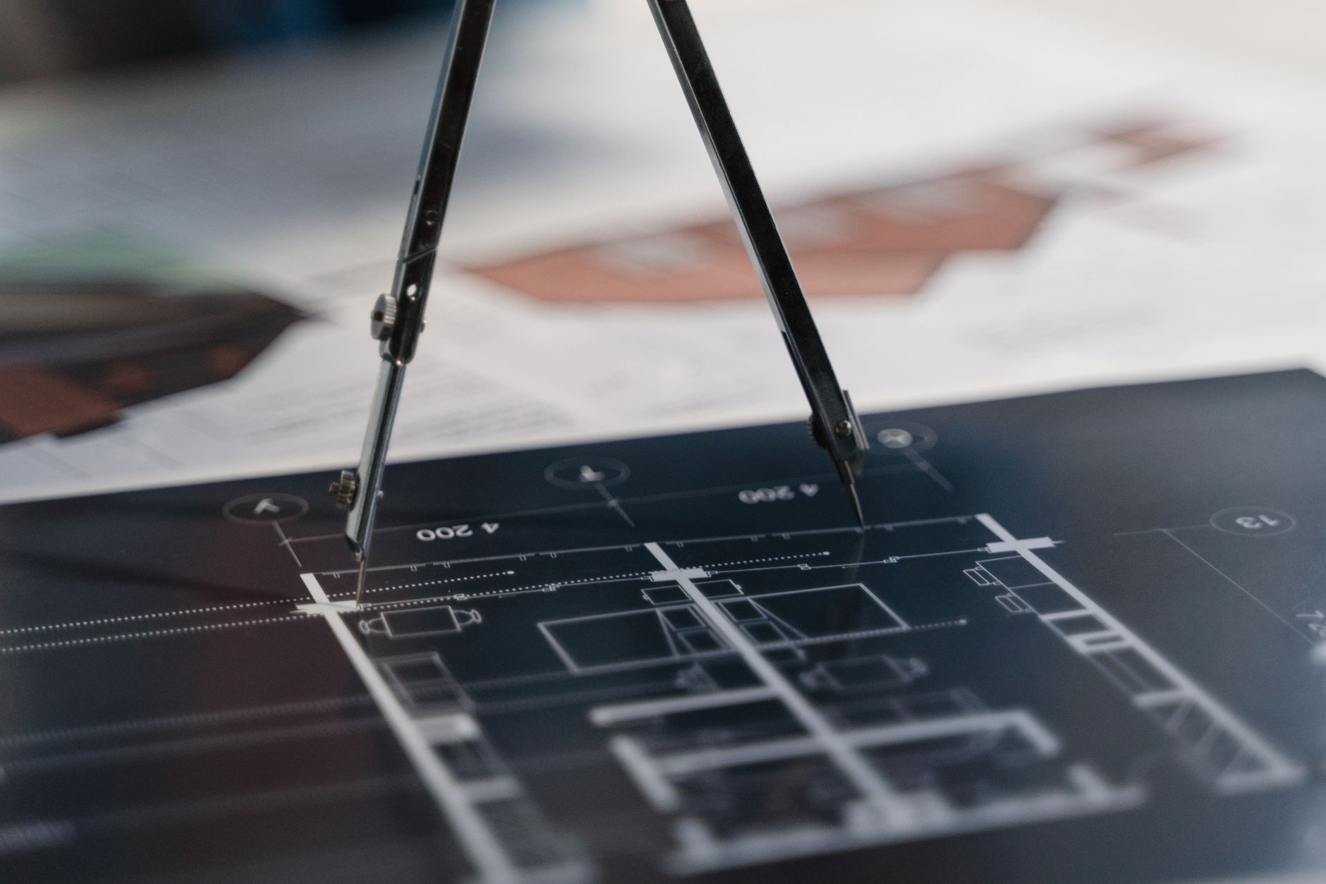 A drafting compass resting on detailed architectural blueprints